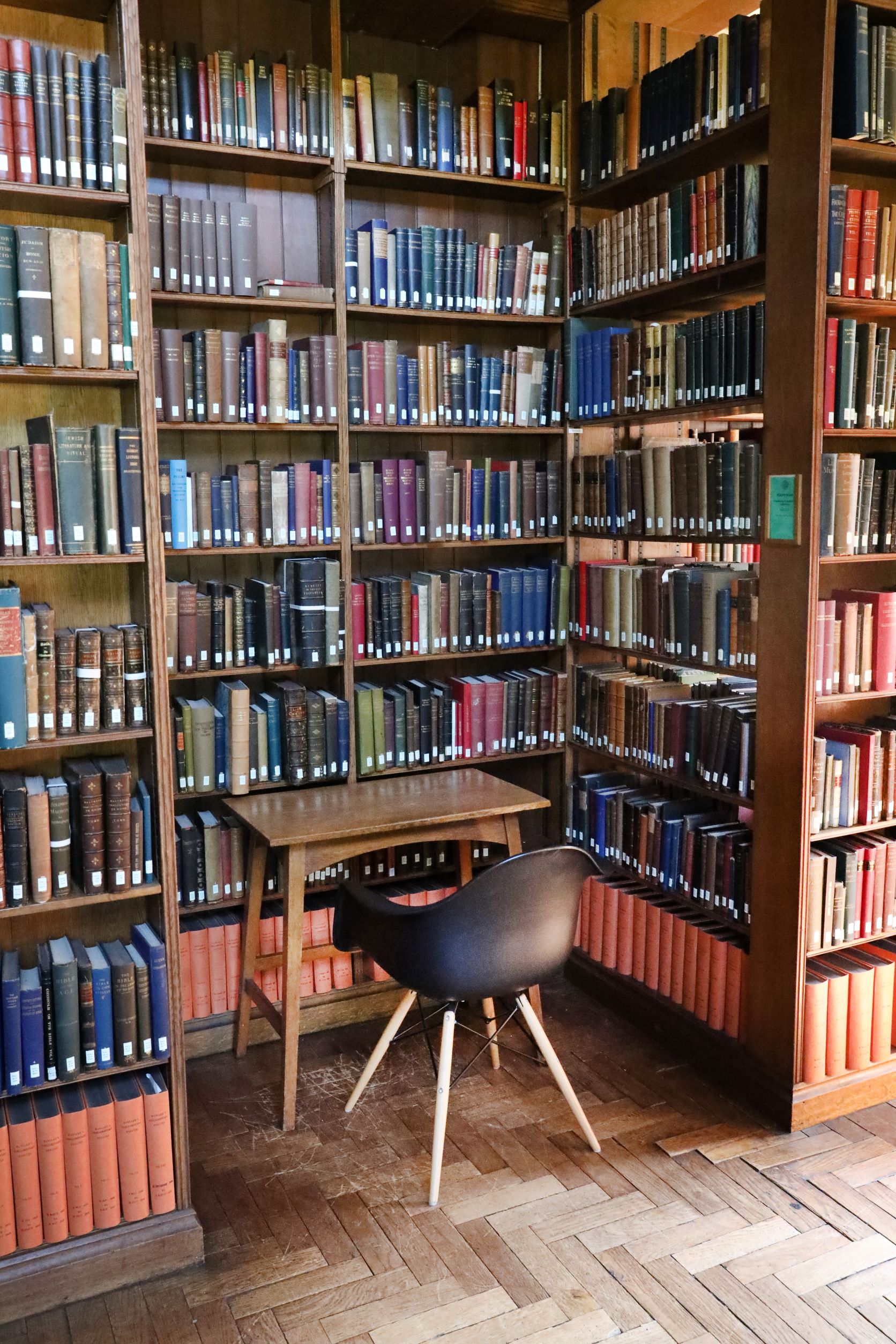 A Reading Room nook between bookshelves. Within the nook there is a wooden desk with a chair. 