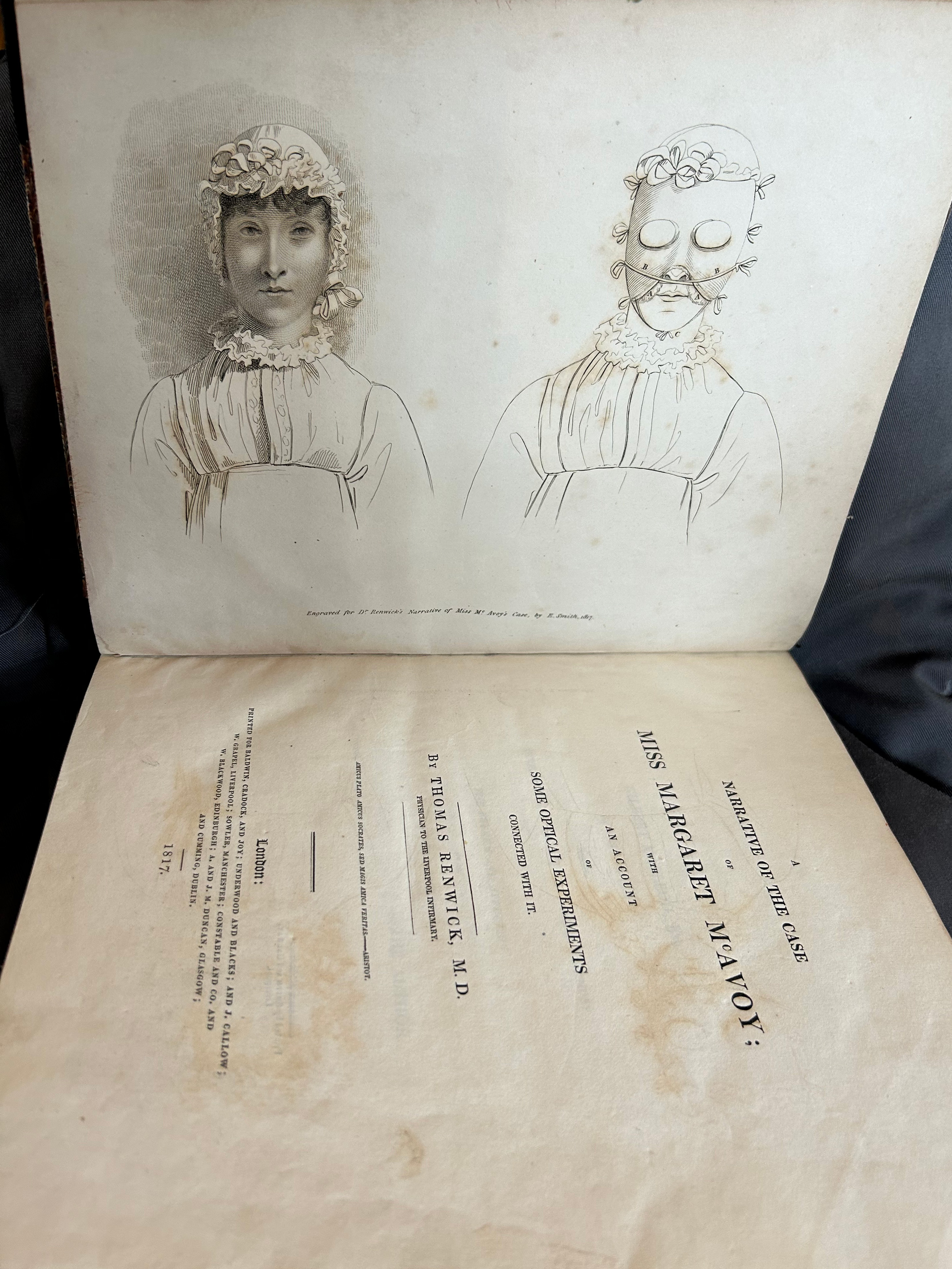 A book held open horizontally. Its title page is visible. The title reads: Miss Margaret McEvoy. There are illustrations on the opposing page showing a rather severe woman looking straight at the viewer next to an image of the the same woman wearing a mask. 